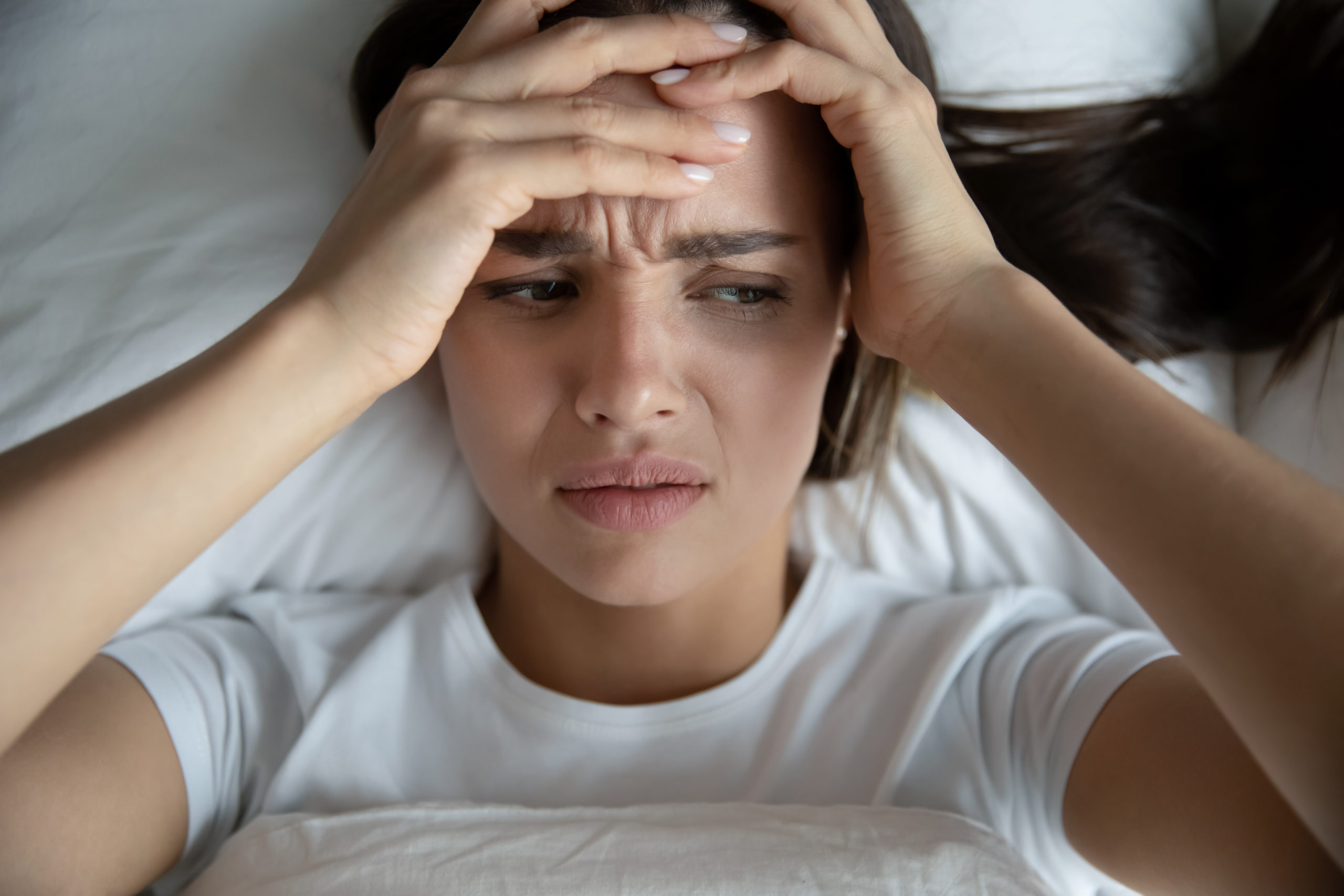 Alkohol Entzugserscheinungen: Frau mit Kopfschmerzen im Bett